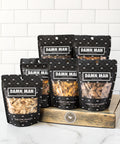 Six bags of "Damn, Man" nuts displayed on a wooden box, featuring a variety of global flavors and classic favorites.