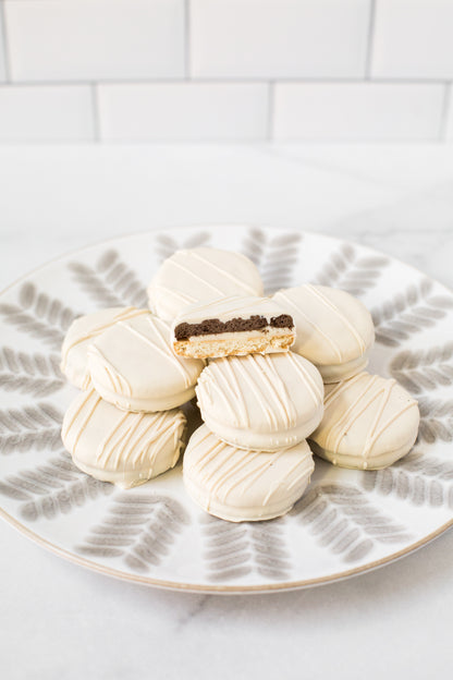 White chocolate-covered sandwich cookies arranged on a decorative plate, with one cookie showing a rich filling.