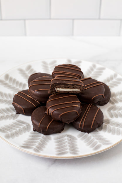 Chocolate-covered sandwich cookies arranged on a plate, showcasing rich, dark chocolate and a creamy filling inside.