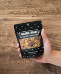 Hand holding Damn Man Tap Room Mix bag with assorted nuts against wooden background