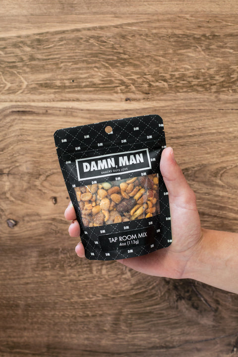 Hand holding Damn Man Tap Room Mix bag with assorted nuts against wooden background