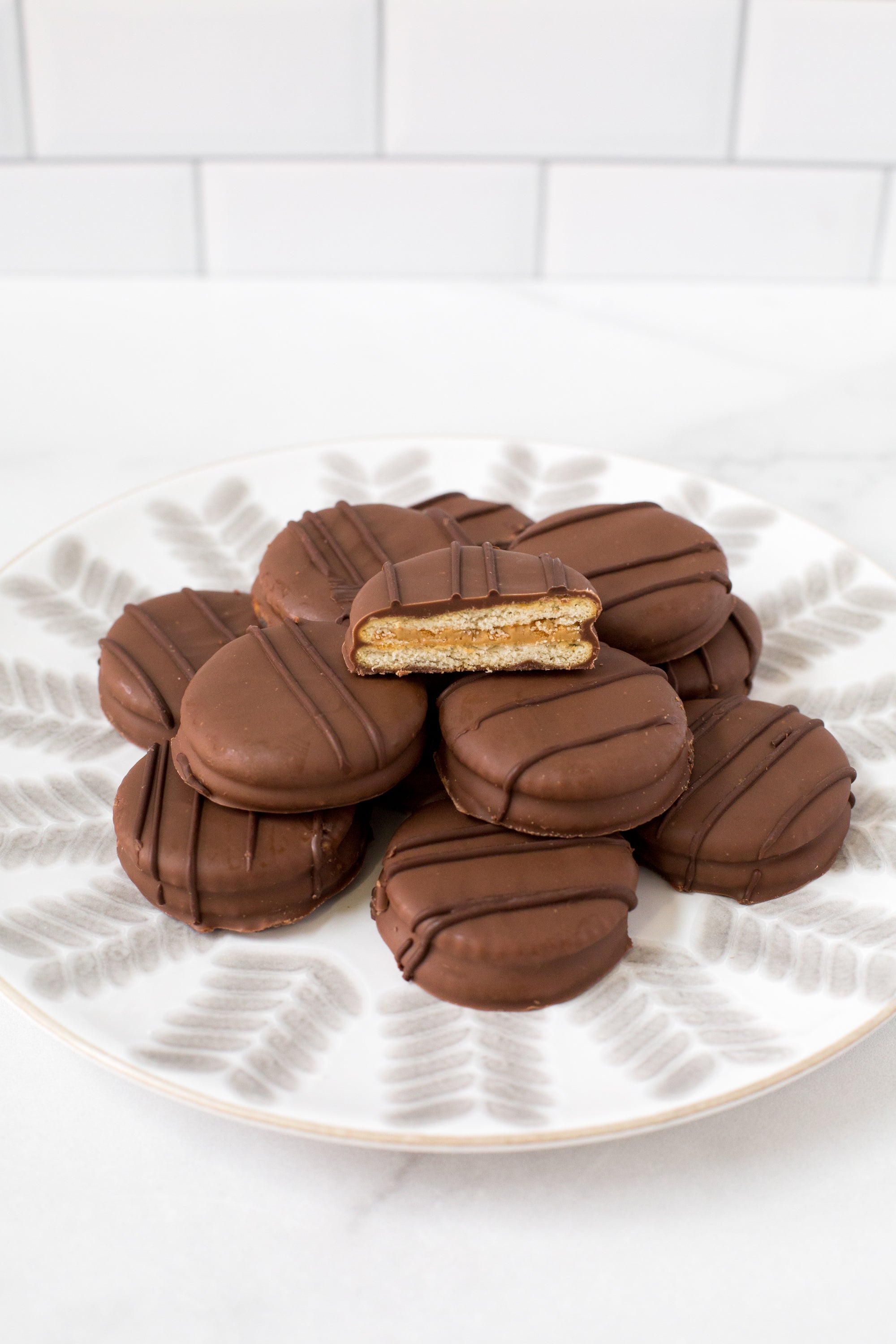 Chocolate-covered peanut butter cracker cookies on a plate, one cookie cut to show creamy milk chocolate coating and filling.