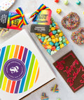 Rainbow box type packaging with the pretzels, gummies, happy birthday chocolate and kettle corn beside. 