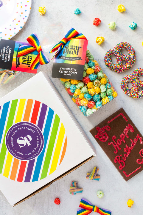 Rainbow box type packaging with the pretzels, gummies, happy birthday chocolate and kettle corn beside. 