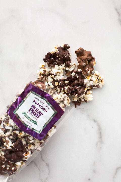 Chocolate-covered popcorn in a clear bag on a marble surface, featuring gourmet popcorn drizzled with milk and dark chocolate.