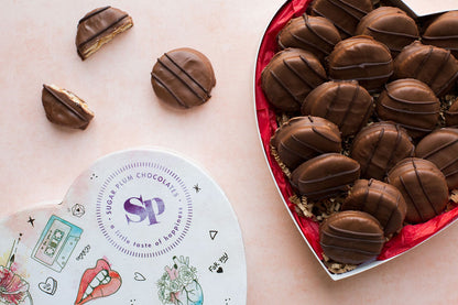 Heart-shaped box of handcrafted milk chocolate-covered peanut butter crackers from Sugar Plum, presented on a light background.