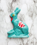 Turquoise bunny wiht red accent color and a white marble background. 