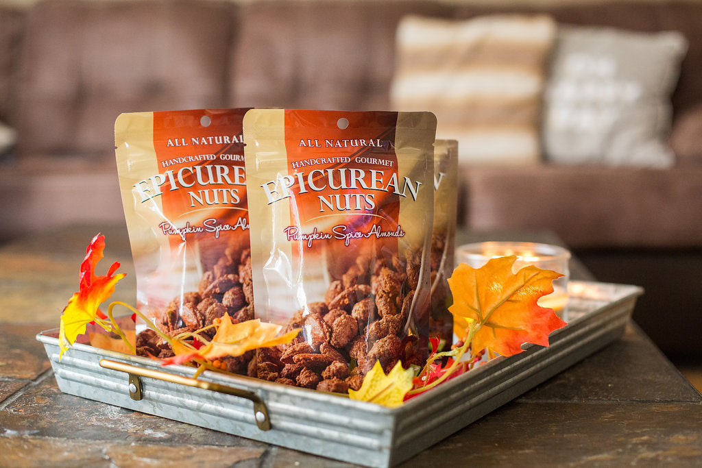 Bags of all-natural Epicurean Pumpkin Spice Almonds on a tray with fall leaves, perfect for seasonal snacking and nut lovers.