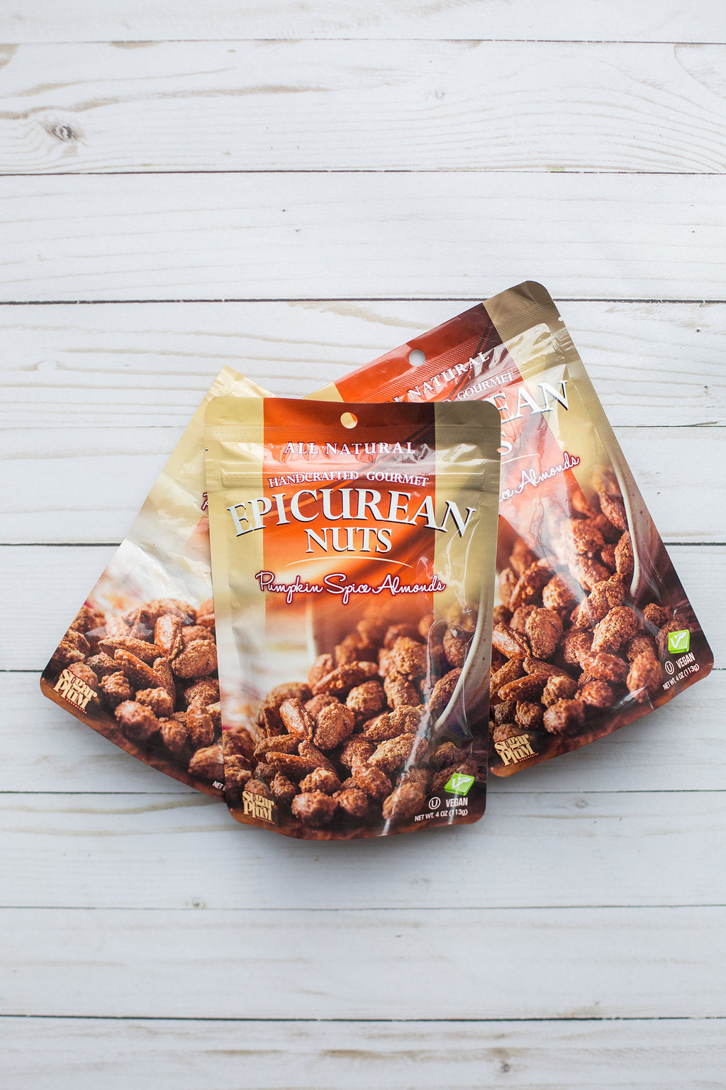 Bags of Epicurean Pumpkin Spice Almonds on a light wood surface.