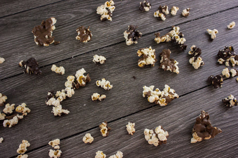 Gourmet chocolate-covered popcorn scattered on a wooden surface, showcasing a sweet and salty snack blend of milk and dark chocolate.