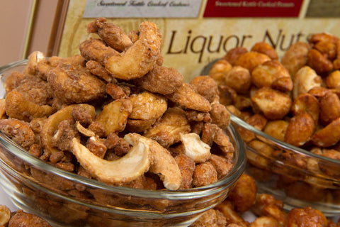 Assorted gourmet nuts with Irish Stout Cashews, Jamaican Lager Peanuts, and Bourbon Almonds in glass bowls from gift tin.
